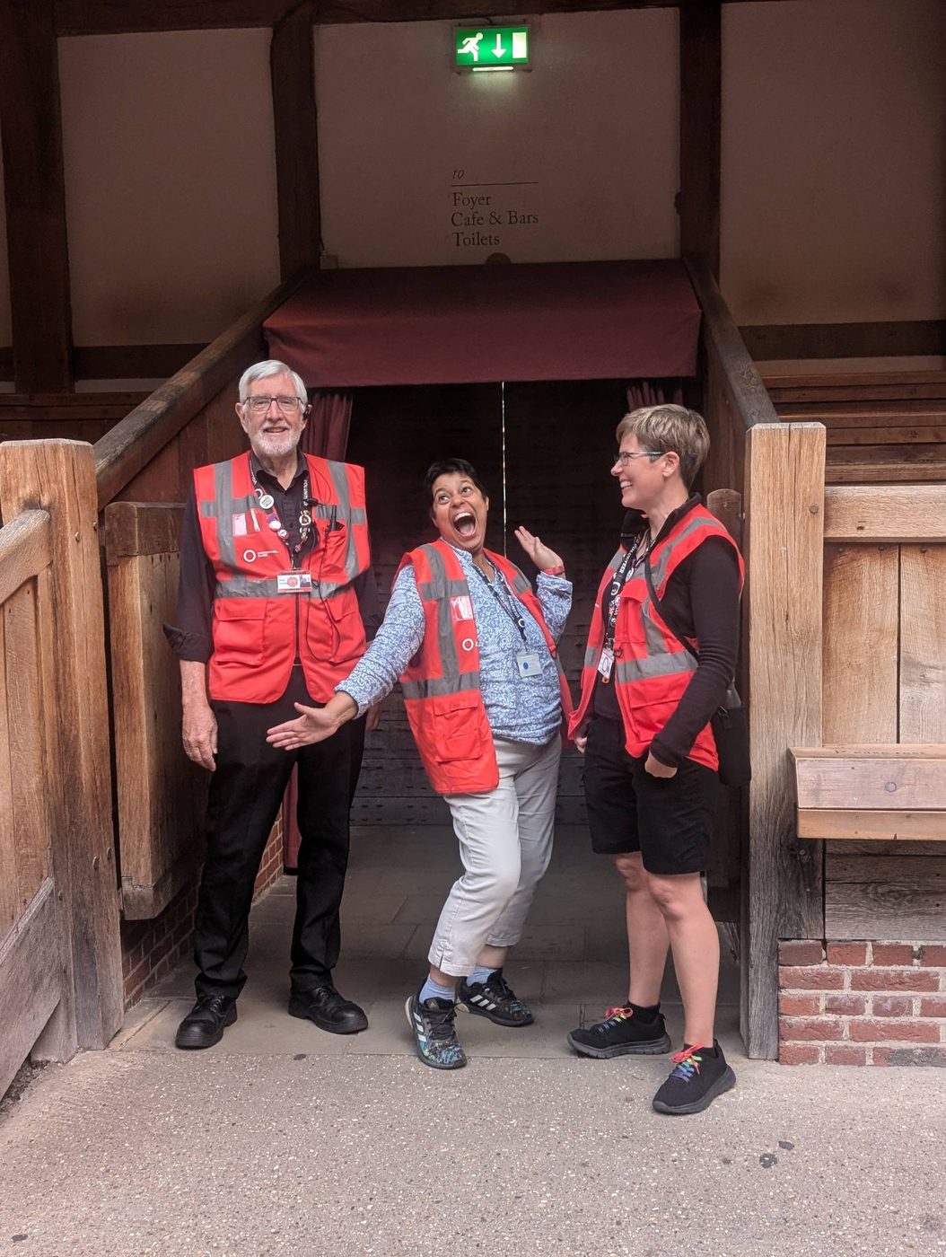 Three volunteer stewards standing at one of the entrances to the Globe Theatre, ready to welcome audience members.