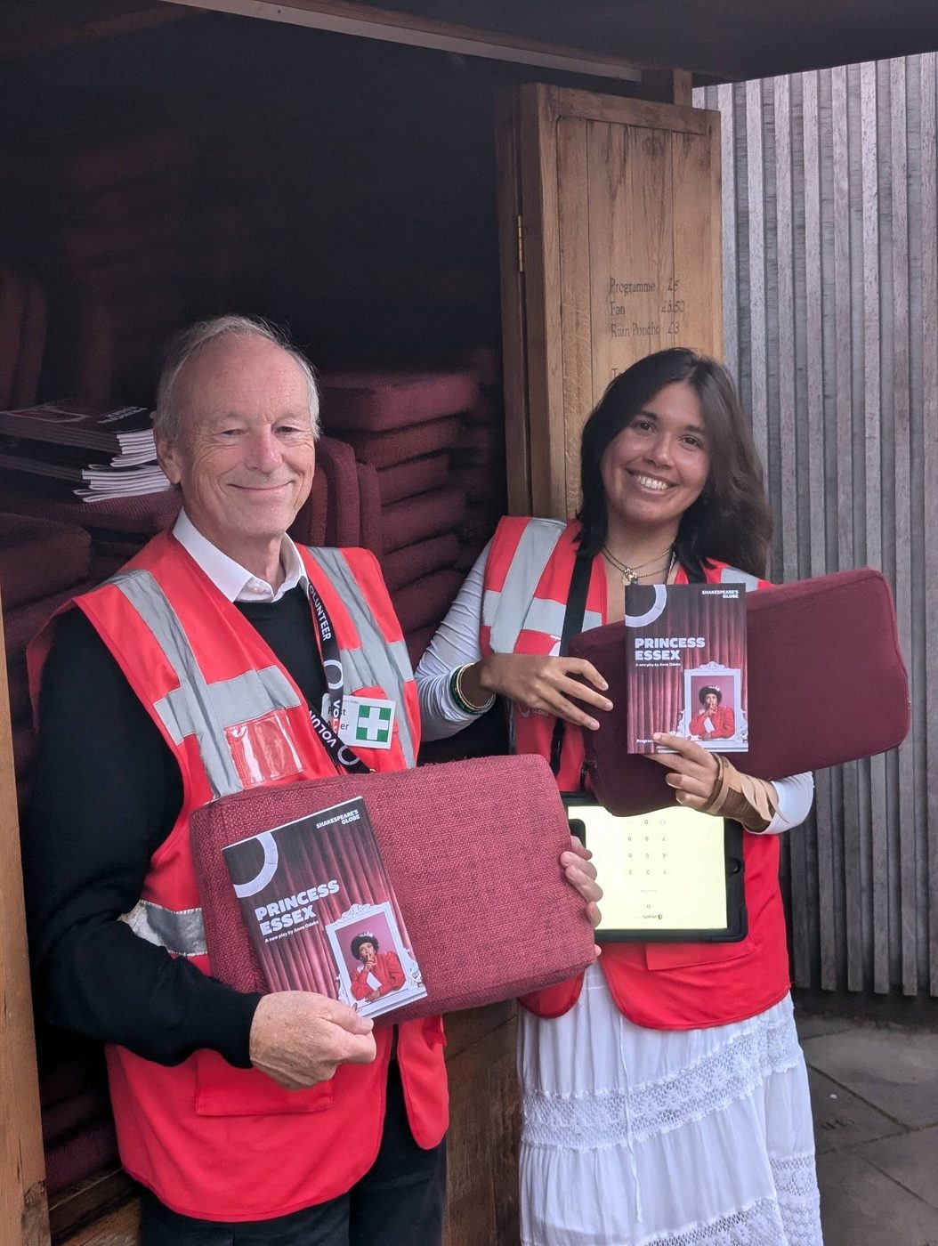 Two volunteer stewards standing at the cushion cart, armed with cushions and programmes to give to audience members.