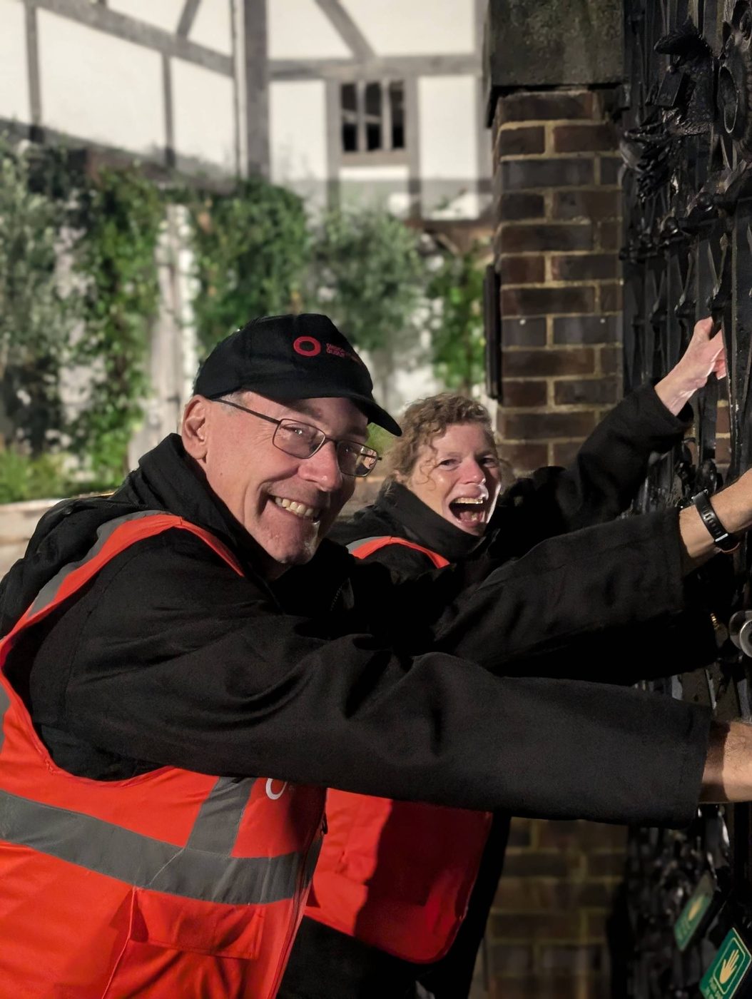 Two smiley volunteer stewards holding on to the entrance gate outside of the Globe Theatre.