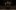 Three lit candles in the dark shadows of an indoor wooden theatre.