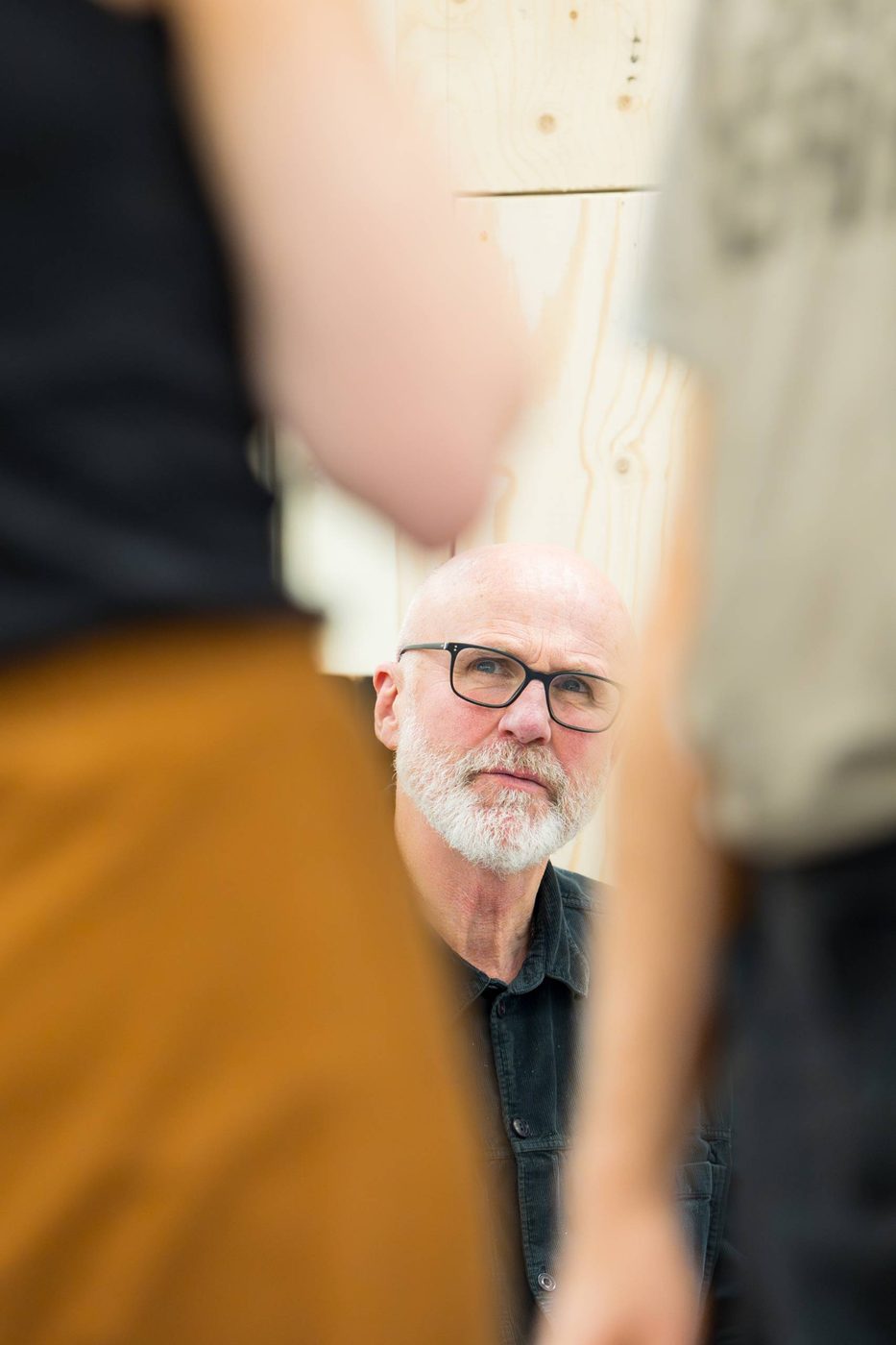 Actor and director Tim Crouch is in-between two blurred bodies in the foreground. He looks up at them.